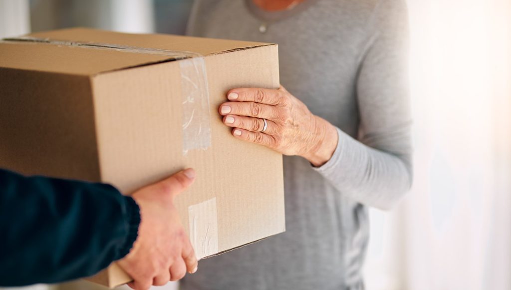 A person handing a sealed cardboard box to another person, representing the final delivery step of DDP shipping.