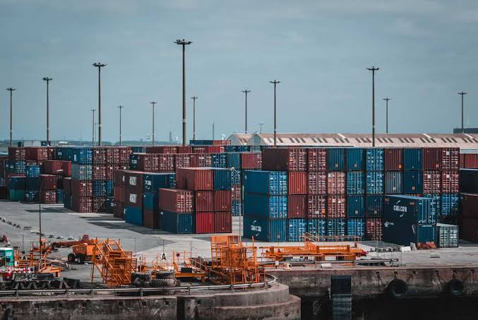 Stacks of colorful shipping containers at a port with orange handling equipment, representing the logistics of 1688 shipping to US.