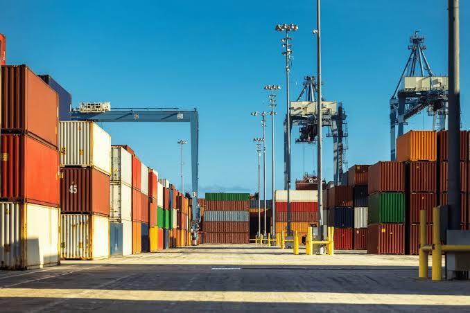 Stacks of colorful shipping containers at a port with blue gantry cranes, representing the logistics of buying from 1688 to US.