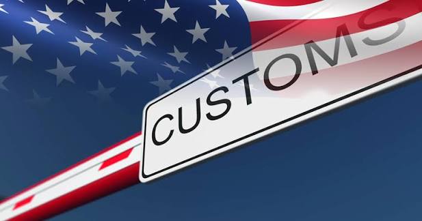 A US Customs sign on a barrier gate with the American flag in the background, representing US customs regulations and import duties.