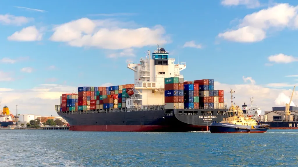 A large container ship loaded with colorful boxes being assisted by a tugboat, representing the process to Consolidate and Ship goods internationally.